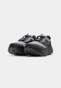 Des chaussures de course noires et grises avec une tige en mesh texturé, dotées d'une semelle en caoutchouc robuste avec un design de tread détaillé et un système de laçage.