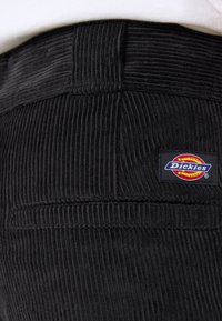 Czarne spodnie typu korduroy z teksturowaną powierzchnią, z widoczną naszywką z logo Dickies na pasku.