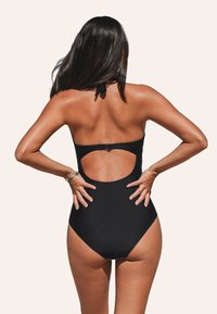 Maillot de bain une pièce noir avec un design à dos découpé, texture lisse et fermeture à clip. Accentué par un lien autour du cou.
