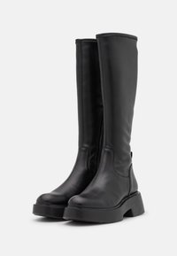 Botas negras hasta la rodilla hechas de cuero suave, con una suela gruesa y robusta, cremallera frontal y un diseño minimalista sin hardware visible.