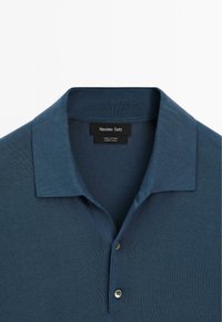 Mørkeblå bomulds polo-shirt med flad krave, tre knaplukninger og en subtil ribbet tekstur. Metalbuttons fuldender designet.