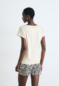 Krämfärgad bomull T-shirt med korta ärmar, tillsammans med svart och vit randiga shorts med zebra-mönster. En enkel och avslappnad design.