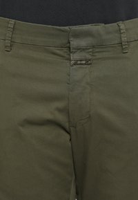 Gros plan sur un pantalon vert olive avec passants pour ceinture et une fermeture avant à languette portant la mention "CLOSED."
