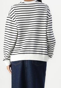 Sudadera de rayas en blanco y negro, con un corte holgado, puños y dobladillo acanalados, y un escote redondo. Combinada con una falda vaquera.