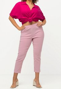 Fuchsia Kurzarmhemd, am Taillenknoten gebunden, kombiniert mit cropped, eng sitzenden rosafarbenen Streifenhosen und beigefarbenen Blockabsatzsandalen.