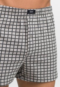 Boxer grigi con un motivo a reticolo nero, realizzati in morbido cotone. Fascia elastica in vita con dettaglio a bottone sul davanti.