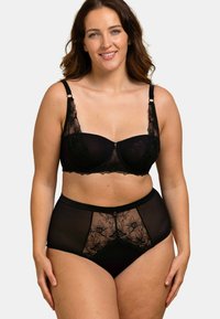 Ensemble de lingerie noire avec un mesh transparent et des accents en dentelle florale. Le soutien-gorge offre un support sous-bust, tandis que les culottes taille haute présentent des détails similaires.