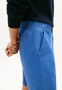 Pantalones cortos azules de tejido suave con un corte ajustado, bolsillos laterales y un pequeño acento con el logo en la parte trasera. Cierre de botón en el bolsillo trasero.