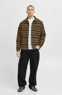 Chaqueta de rayas marrón y beige con cierre de botones en el frente, bolsillo lateral, usada sobre una camisa blanca, combinada con pantalones amplios negros y zapatillas grises.
