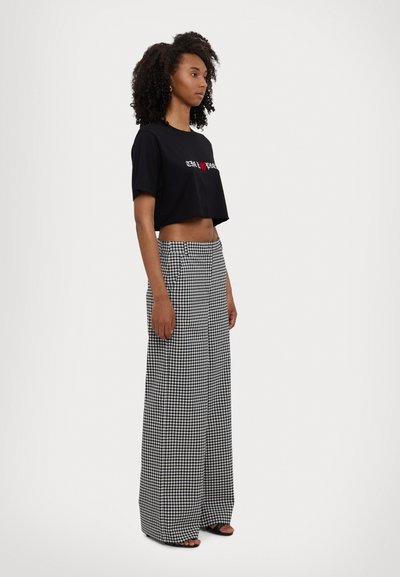 Zwarte cropped t-shirt met witte en rode tekst, gecombineerd met hoge taille wijde broek in een zwart-wit ruitpatroon.