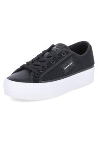 Sneaker noir avec un dessus texturé en tissu noir et cuir, doté d'une semelle plateforme blanche, de lacets noirs et d'une étiquette de logo sur le côté.