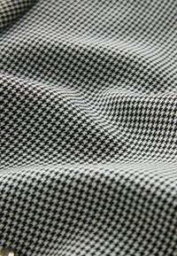 Zwart-witte houndstooth-gepatroneerde stof met een gestructureerd oppervlak, die soepele, vloeiende plooien vertoont en een consistent geometrisch ontwerp.