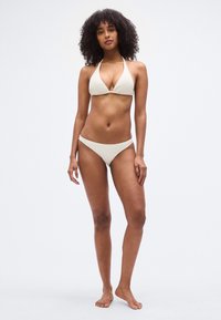 Σετ μπικίνι με μπεζ τριγωνικό τοπ με λαιμόκοψη halter και σλιπ με χαμηλή γραμμή, με υφασμάτινη υφή και μινιμαλιστικό σχεδιασμό.
