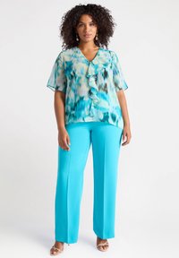 Una blusa trasparente e decorata in teal e azzurro chiaro con volant lungo il davanti, abbinata a pantaloni larghi turchesi.