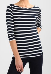 Granatowo-biały top w paski z długim rękawem, dekoltem typu łódka i delikatnym wycięciem łódkowym. Miękki, elastyczny materiał, dopasowany krój i boczne rozcięcia.