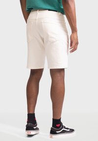 Helle Denim-Shorts mit geradem Schnitt, sichtbaren Gesäßtaschen und ausgefransten Säumen, kombiniert mit schwarzen Turnschuhen und gemusterten Socken.