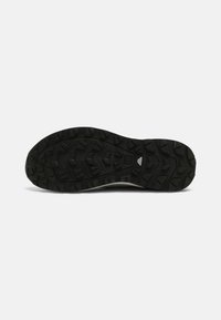 Black rubber shoe sole with deep tread and traction patterns. Textured surface and angular protrusions for grip and stability.