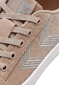 Beżowe tekstylne sneakersy z srebrnym haftem, teksturowana powierzchnia, okrągłe sznurówki, gumowa podeszwa oraz metka z logo na górze.