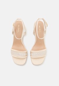Sandales beige Aldo avec brides à la cheville, talons blocs bas et bandes avant texturées avec coutures décoratives.