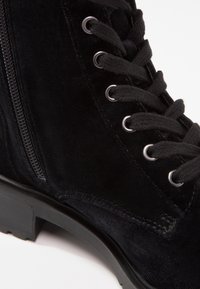 Botte à lacets en daim noir avec semelle épaisse en caoutchouc et fermeture éclair latérale, dotée d'œillets métalliques et de détails cousus.