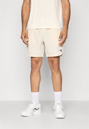 Beige athletic shorts with a blue logo, designed for comfort. Worn with white socks and sports shoes, featuring a casual fit.