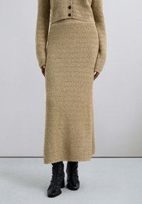 Compleu tricotat format din două piese, care include un cardigan scurt cu nasturi și o fustă lungă cu model zigzag în nuanțe de bej, accesorizată cu cizme negre cu toc.