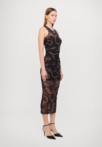 Black dress with pink floral patterns, form-fitting design, sleeveless. Sheer lower half, paired with black pointed-toe heels and ankle straps.