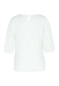 Blouse blanche avec broderie ajourée, manches trois-quarts bouffantes, et une petite fermeture à bouton en forme de goutte d'eau à l'arrière du col.