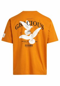 T-shirt en coton orange avec un col rond. Présente un graphisme de colombes blanches, le texte "GRACIEUX" et un code-barres au dos.