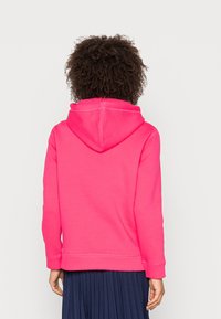 Roze hoodie met capuchon, geribbelde boorden en zoom. Gemaakt van zacht materiaal; bevat een eenvoudig ontwerp met zichtbare stiksels.