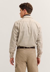 Camicia a scacchi beige, con dettagli del colletto in blu navy. Tessuto morbido, maniche lunghe e vestibilità classica, abbinata a pantaloni marrone chiaro.
