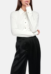 White long-sleeve button-up shirt with a collar, featuring silver button accents, paired with black satin wide-leg pants. Smooth texture.