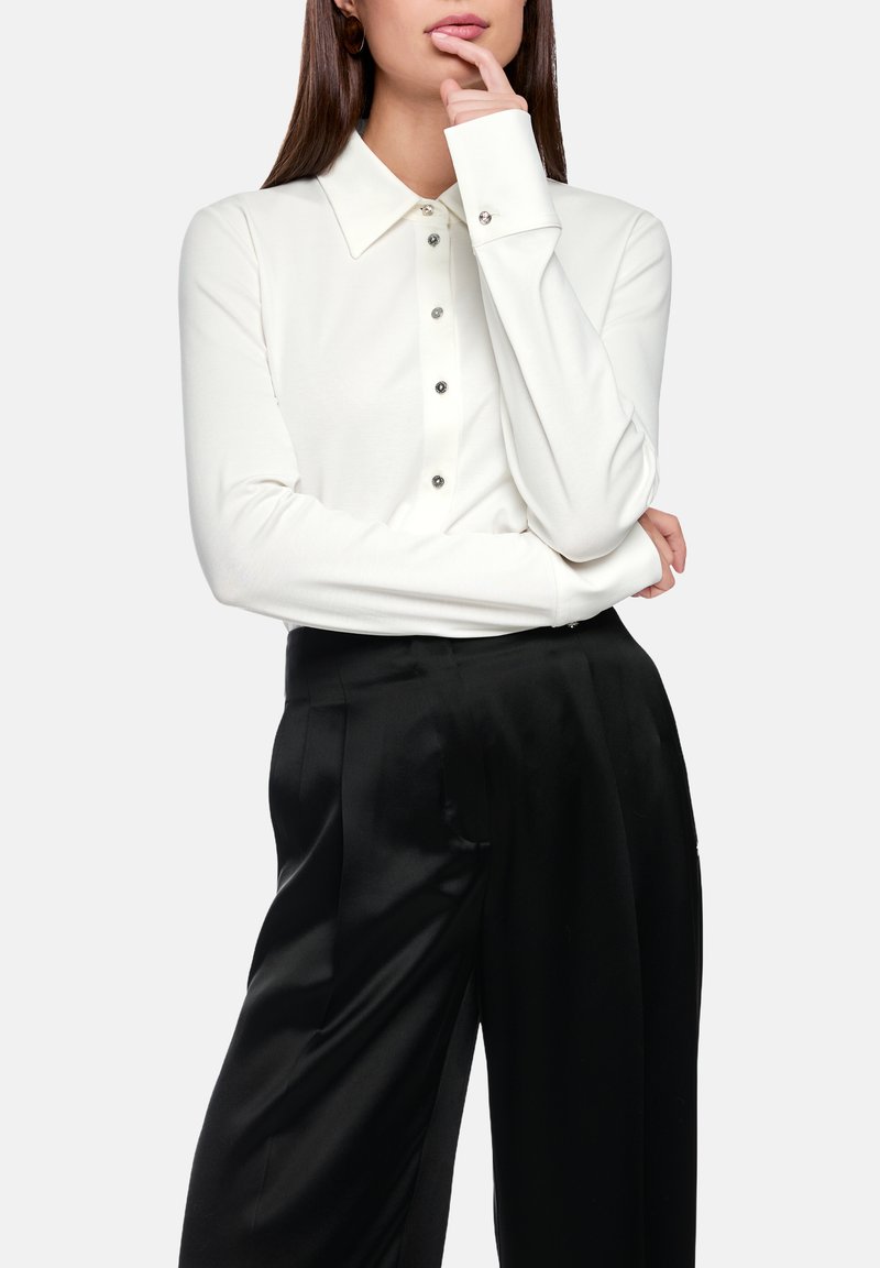 White long-sleeve button-up shirt with a collar, featuring silver button accents, paired with black satin wide-leg pants. Smooth texture.