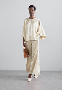 Light beige satin top and wide-leg trousers, featuring a loose fit, subtle sheen, and minimalistic design. Accessorized with a perforated tote.
