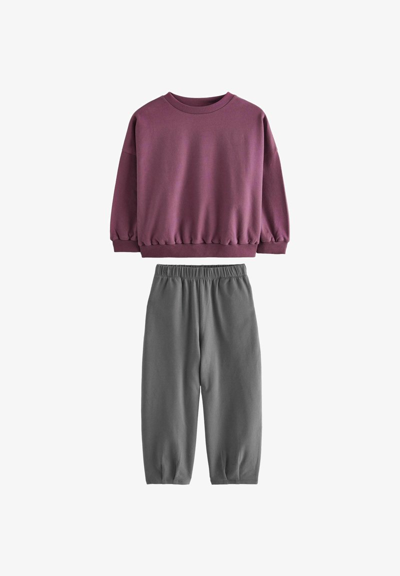 Fioletowa bluza z elastycznymi mankietami i dołem, zestawiona z szarymi spodniami o zwężanym kroju z elastycznym pasem. Miękka tkanina o gładkiej fakturze.