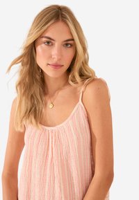 Top in rosa chiaro con strisce verticali testurizzate, spalline sottili e scollatura arricciata. Indossato da una modella con capelli lunghi.