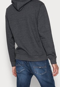 Felpa grigia scura con cappuccio, con polsini e orlo a coste, abbinata a jeans blu con due tasche posteriori e un design cucito.