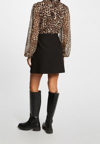 Sort nederdel med høj talje; gennemsigtig bluse med leopardprint og lange ærmer; knæhøje sorte læderstøvler med kraftige såler.