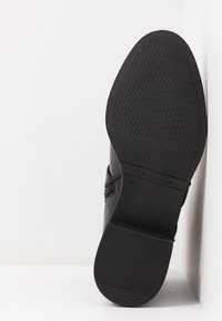 Zapato negro con suela de goma texturizada, parte superior de cuero suave y cremallera lateral. Presenta la marcación de talla "37" y el nombre de la marca "Tamaris."