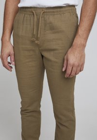 Pantalones drawstring color caqui, fabricados con un tejido ligero, que presentan un fit relajado, una superficie texturizada y sutiles detalles de costura lateral.