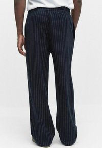 Marinblå randiga vida byxor gjorda av mjukt tyg, med en platt midjeband och två sidorfickor.