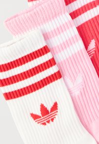 Τρία ζευγάρια ραβδωτά κάλτσες σε λευκό με κόκκινες ρίγες, ροζ με λευκές ρίγες, και κόκκινο με ροζ ρίγες, το καθένα με λογότυπο τριφυλλιού.