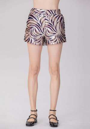 Femme portant un short taille haute violet et beige à motifs avec des chaussures à talons blocs noires à brides, montrée du ventre jusqu'aux pieds.