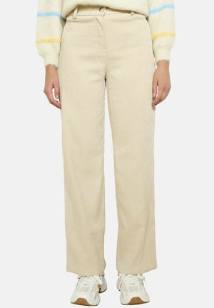 Beige Cord-Hosen mit weitem Bein, versehen mit strukturierten vertikalen Streifen und einem frontalen Knopfverschluss, kombiniert mit weißen Sneakern.