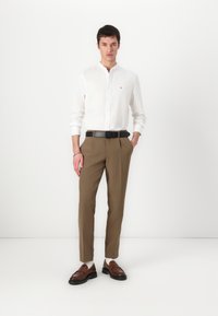 Camicia bianca a maniche lunghe con bottoni, pantaloni marroni su misura, cintura nera e mocassini marroni. Design semplice, texture liscia e forma aderente.