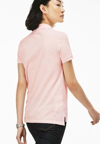 Kortärmad rosa polo med texturerad tyg, klassisk krage och sidospalttor, i kombination med mörka denimjeans.