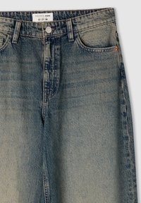 Jeans in denim azzurro chiaro con una leggera scoloritura, dotati di chiusura frontale con bottone, cinque tasche e un'etichetta sulla vita.