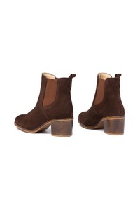 Botines de ante marrón con paneles laterales elásticos, puntera redondeada y tacón apilado. Incluyen una pestaña en la parte trasera para facilitar el uso.