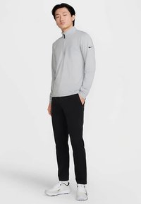 Szürke sportos pulóver fél cipzáros kivitelben, hosszú ujjakkal és Nike logóval a bal vállon. Fekete nadrággal és fehér cipővel párosítva.