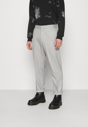 Lysegrå skræddersyede bukser med opkrogede kanter og en glat tekstur. Kombineret med sorte ankelstøvler og en sort tie-dye bluse med lange ærmer.